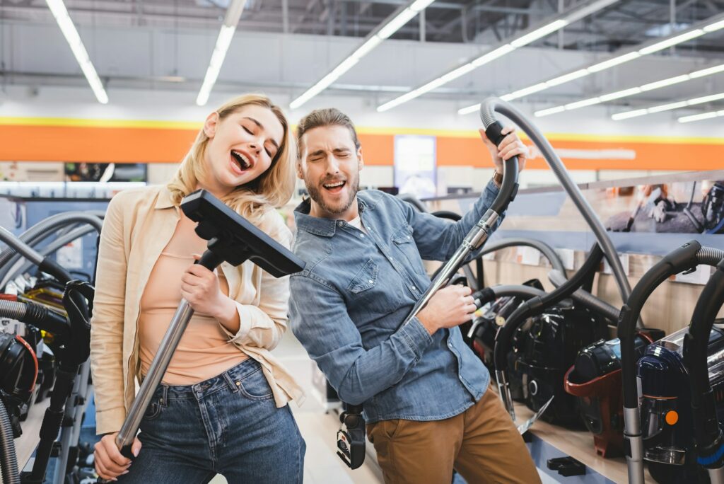 boyfriend playing with vacuum cleaner and girlfriend singing in home appliance store